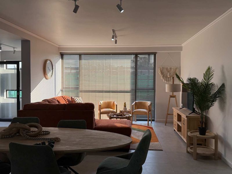 Spacious open-plan living and dining area featuring modern track lighting, large windows with venetian blinds, and neutral tiled flooring throughout.