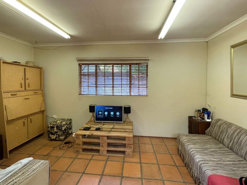 A living room featuring terracotta tiled flooring, venetian blinds, and fluorescent strip lighting, offering a functional space with potential for modernization.