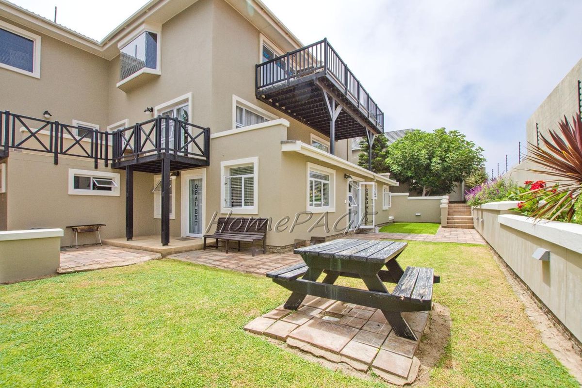 Rear exterior view of the guest house featuring a landscaped garden, paved patio areas, and elevated wooden balconies accessible from the upper levels.