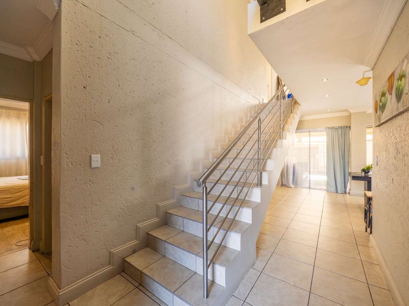 A bright hallway featuring a tiled staircase with a modern stainless steel balustrade, leading to an open living area with ceramic floor tiles.