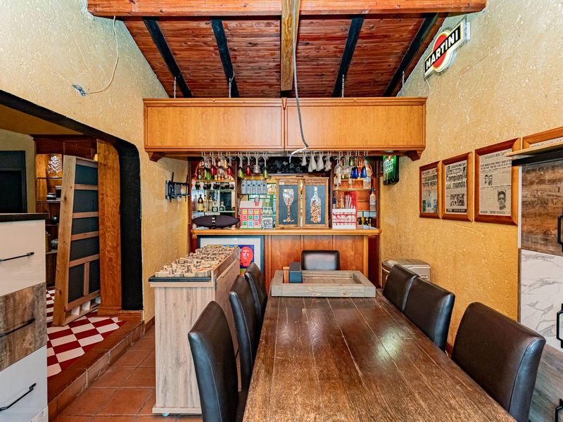 A rustic-style home bar area featuring a built-in counter, exposed timber ceiling beams, and tiled flooring, offering a dedicated space for entertaining.