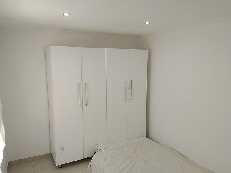 A bedroom featuring a large white built-in wardrobe, tiled flooring, and recessed ceiling downlights.