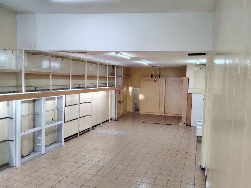An empty commercial retail space featuring tiled flooring, built-in wall shelving, and fluorescent lighting, ready for renovation or new business fit-out.