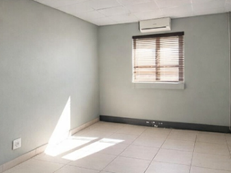 A vacant office space featuring tiled flooring, a drop ceiling, an integrated air conditioning unit, and a window with fitted venetian blinds.