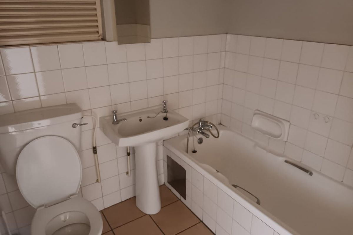 A dated bathroom featuring a pedestal basin, toilet, and bathtub with white wall tiling and tiled flooring.