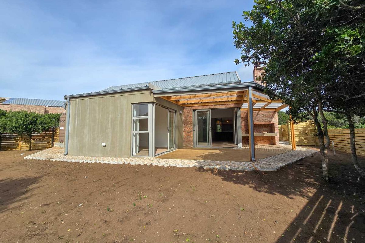 Rear view of the townhouse featuring a wooden deck, covered patio with built-in braai, and sliding door access to the interior living space.