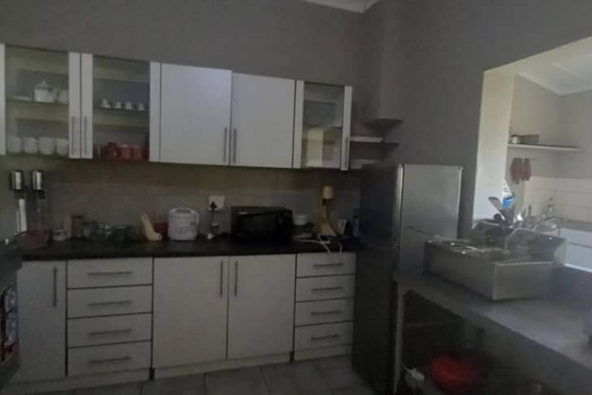 A functional kitchen featuring white cabinetry, dark countertops, and tiled flooring, with an adjacent scullery area visible through the opening.