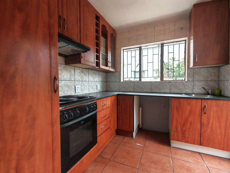 A functional kitchen featuring wood-finish cabinetry, built-in oven with extractor, tiled backsplash, and tiled flooring, offering a practical layout for renovation.