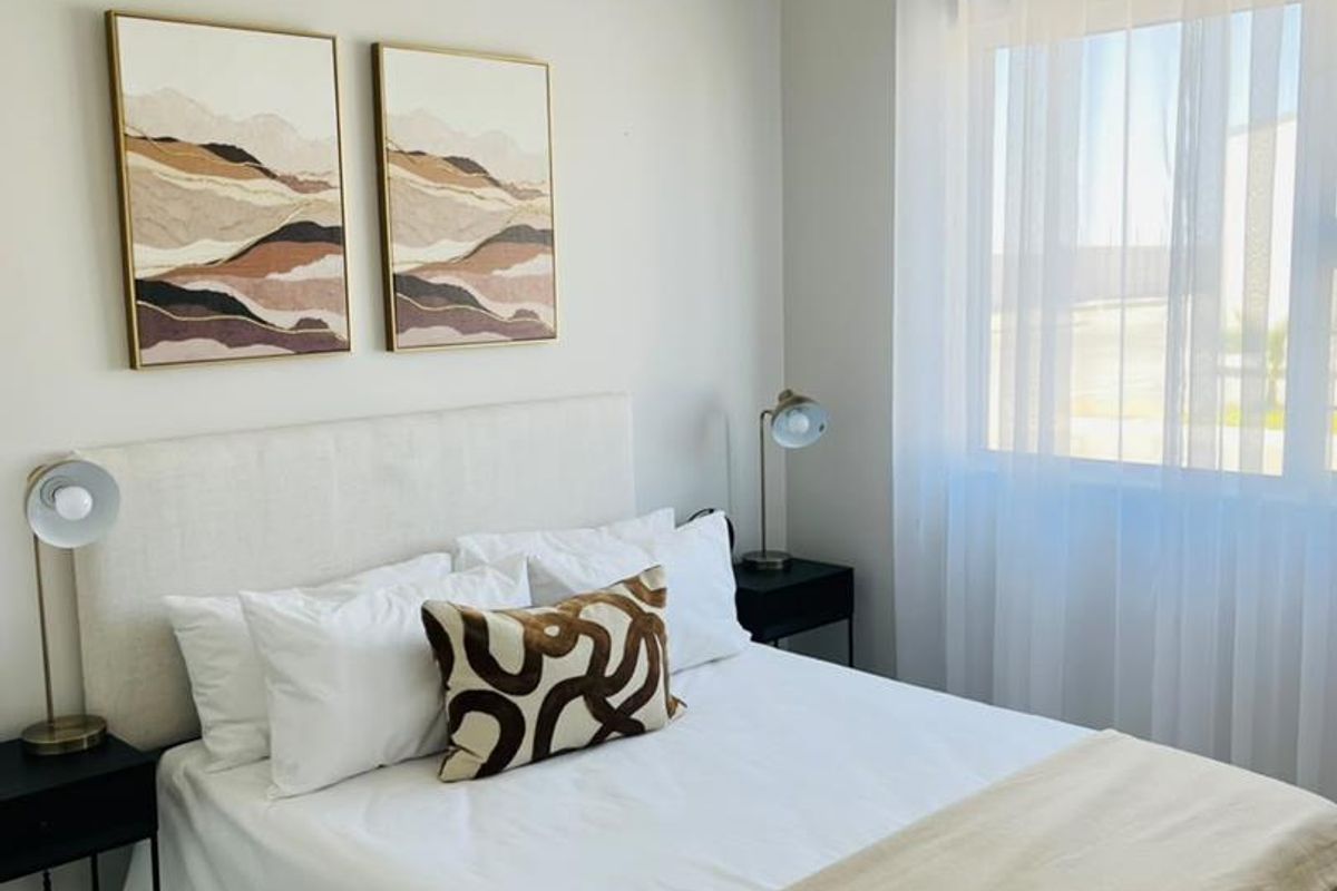 A well-maintained bedroom featuring neutral wall tones, a window with sheer curtains, and a classic tongue and groove ceiling finish.