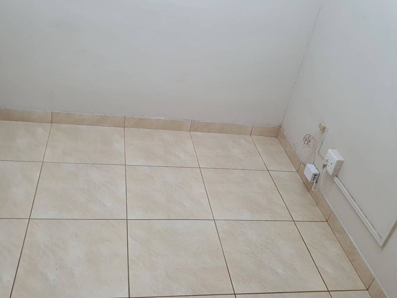 A small, empty office space featuring neutral ceramic floor tiles and wall-mounted electrical points.