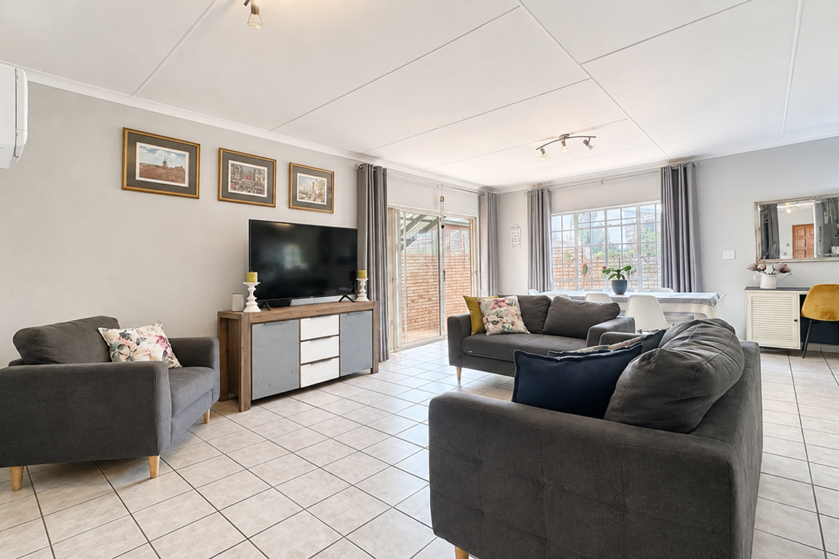 A bright and spacious living room featuring neutral tiled flooring, coved ceilings, and a sliding glass door providing access to the outdoor area.