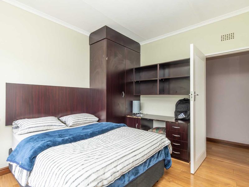 A bedroom featuring built-in dark wood cabinetry, including a wardrobe, desk, and shelving unit, complemented by laminate flooring.