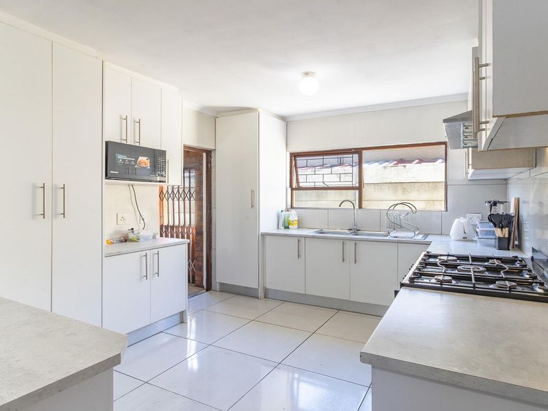 A functional kitchen featuring white cabinetry, a gas hob with extractor, built-in microwave, and tiled flooring, providing a clean and practical workspace.