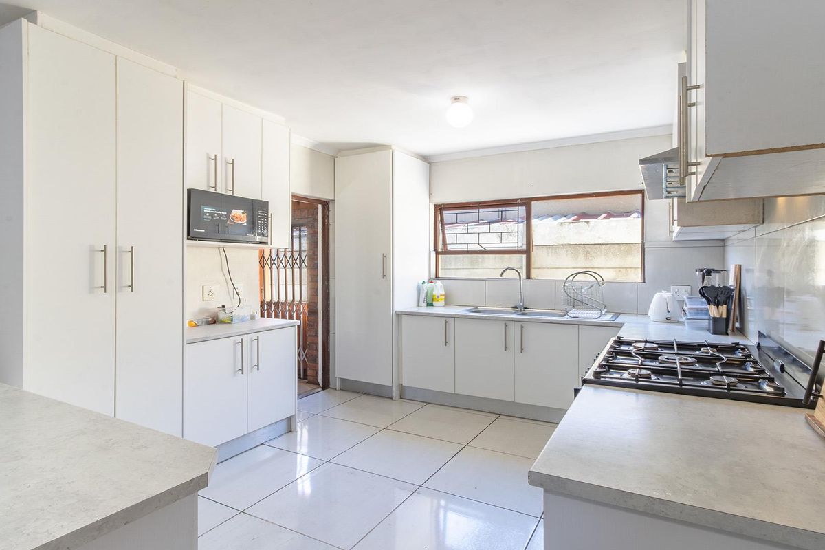A functional kitchen featuring white cabinetry, a gas hob with extractor, built-in microwave, and tiled flooring, providing a clean and practical workspace.