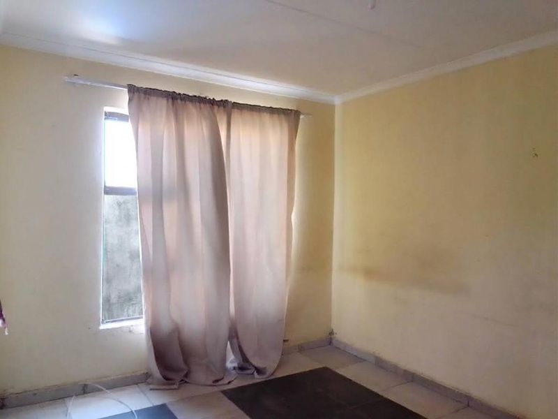 An empty bedroom featuring tiled flooring and a window with a curtain rod, requiring cosmetic updates to the wall finishes.