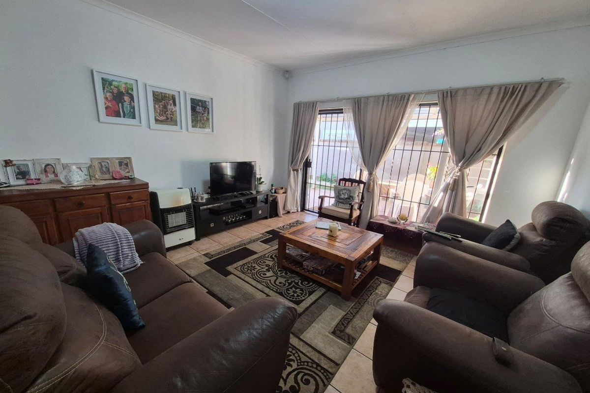 A comfortable living room featuring tiled flooring and large sliding glass doors with security bars, providing direct access to the outdoor area.