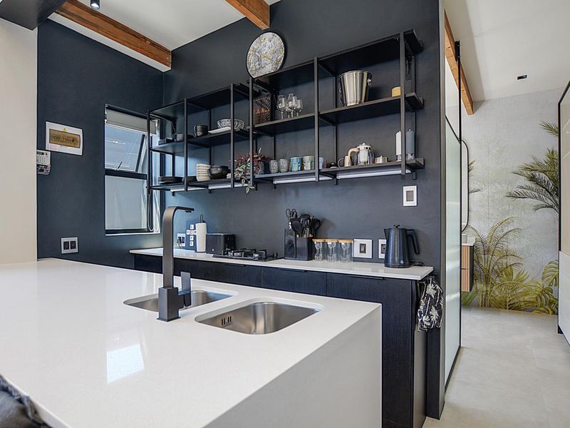 Modern kitchen featuring a sleek quartz island with double undermount sink, black fixtures, gas hob, and stylish open shelving against a dark feature wall.