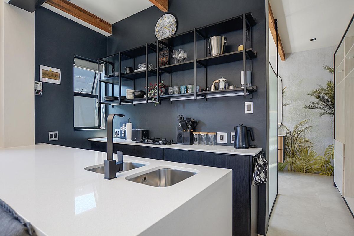 Modern kitchen featuring a sleek quartz island with double undermount sink, black fixtures, gas hob, and stylish open shelving against a dark feature wall.