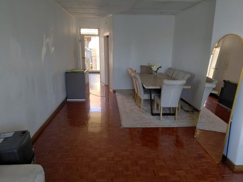A living and dining area featuring traditional parquet flooring and plain white walls, requiring minor cosmetic updates to improve the overall aesthetic.