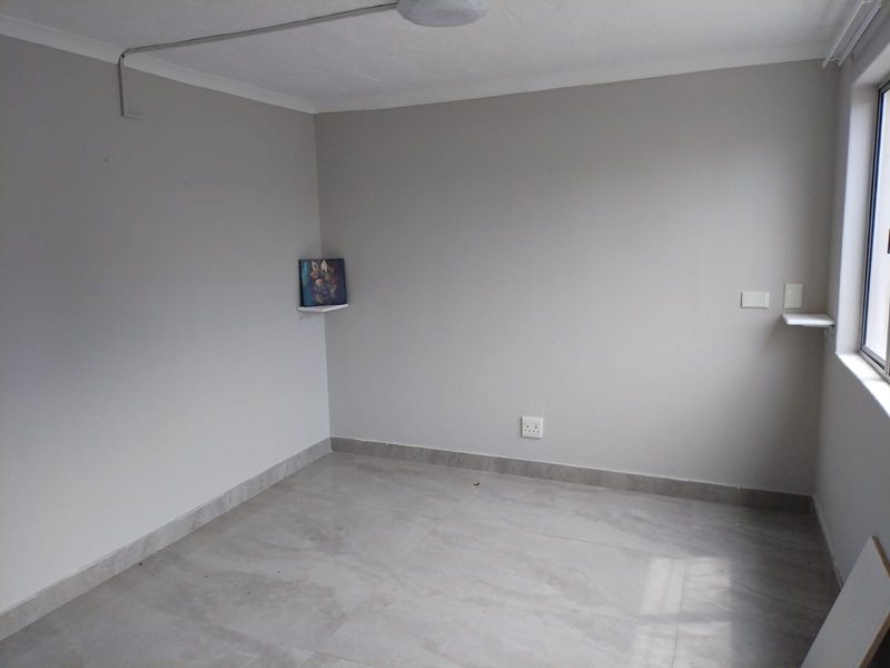 An empty bedroom featuring neutral grey walls, tiled flooring, and surface-mounted electrical conduit, offering a clean canvas for interior design.
