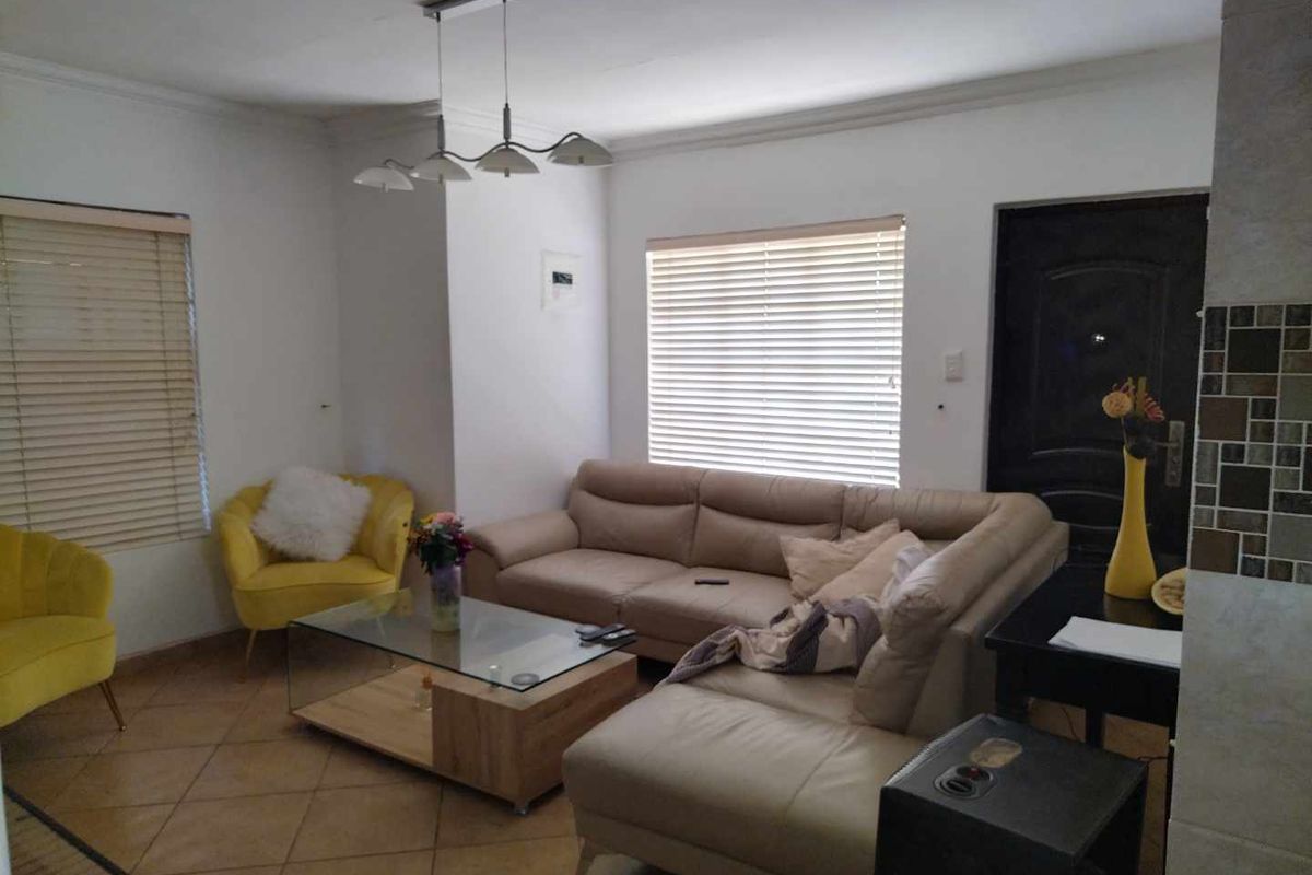 A living room featuring tiled flooring, venetian blinds, and a modern pendant light fixture, providing a functional and well-lit space.