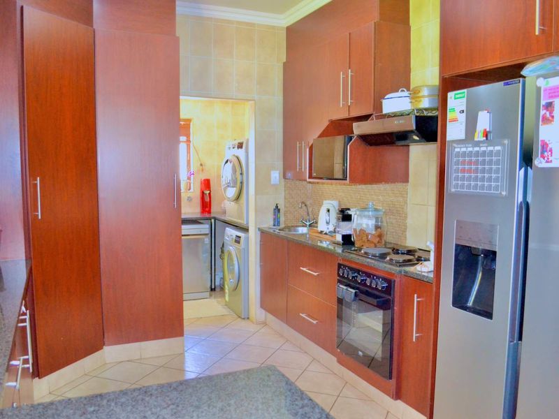 A functional kitchen featuring dark wood cabinetry, granite countertops, built-in appliances, and a tiled backsplash, with an adjacent scullery area visible.