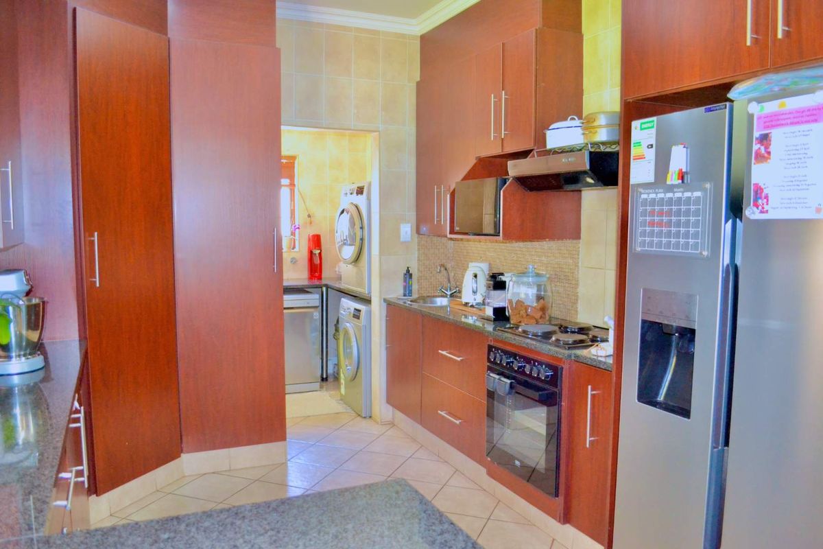 A functional kitchen featuring dark wood cabinetry, granite countertops, built-in appliances, and a tiled backsplash, with an adjacent scullery area visible.
