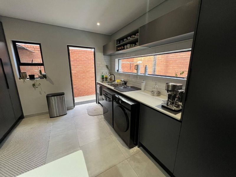 Modern, well-appointed scullery featuring sleek dark cabinetry, stone countertops, subway tile backsplash, and integrated appliances with direct access to an outdoor courtyard.