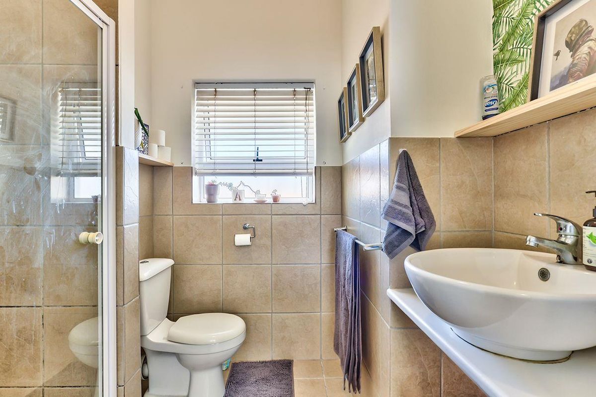 A compact, well-maintained bathroom featuring a glass shower enclosure, a modern vessel sink, and neutral wall tiling.