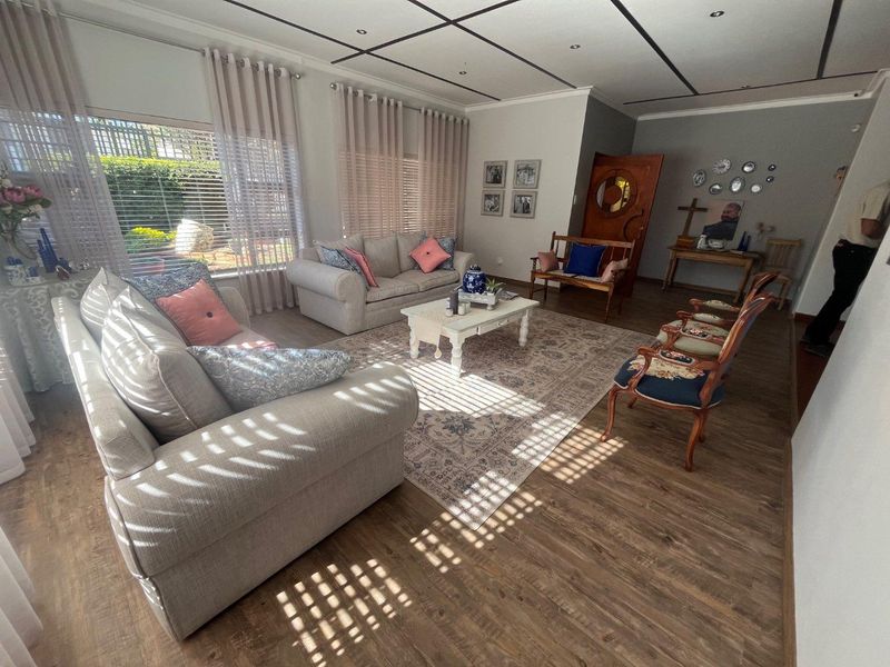 A spacious living room featuring laminate flooring, recessed downlighting, and large windows with venetian blinds, offering a bright and comfortable atmosphere.