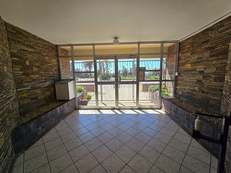 A secure apartment building entrance featuring stone-clad walls, tiled flooring, and large glass panels with security gates leading to the exterior.