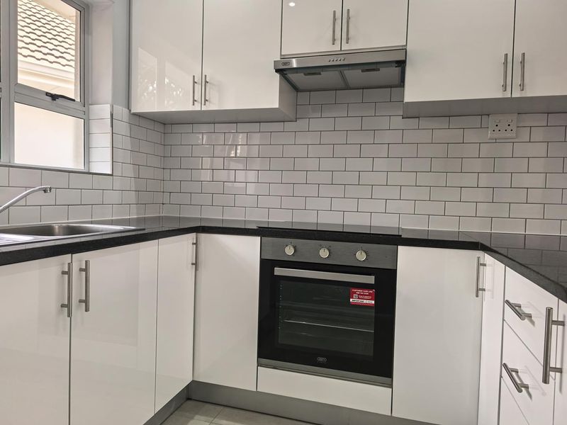 Modern kitchen featuring white gloss cabinetry, black granite countertops, subway tile backsplash, and integrated stainless steel appliances.