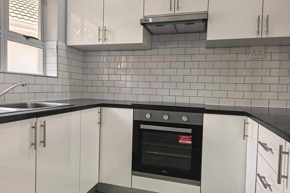 Modern kitchen featuring white gloss cabinetry, black granite countertops, subway tile backsplash, and integrated stainless steel appliances.