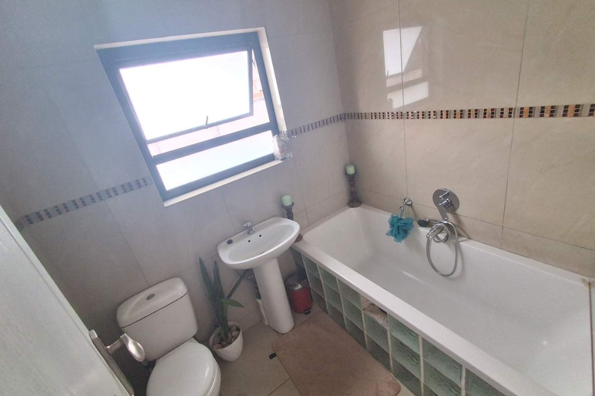 A functional bathroom featuring a pedestal basin, a standard toilet, and a bathtub with a glass block surround and wall-mounted shower mixer.