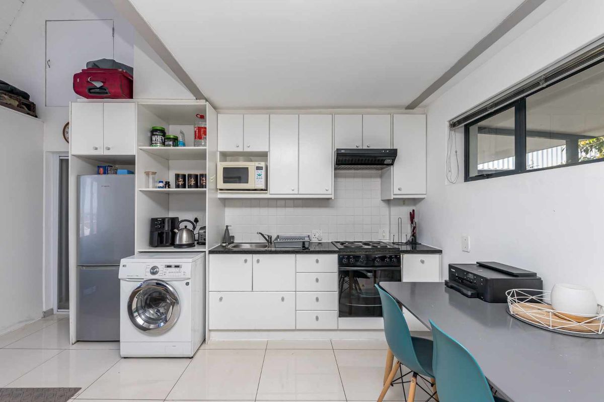 Compact kitchen featuring white cabinetry, dark countertops, integrated oven and hob, extractor fan, and a dedicated space for a washing machine.