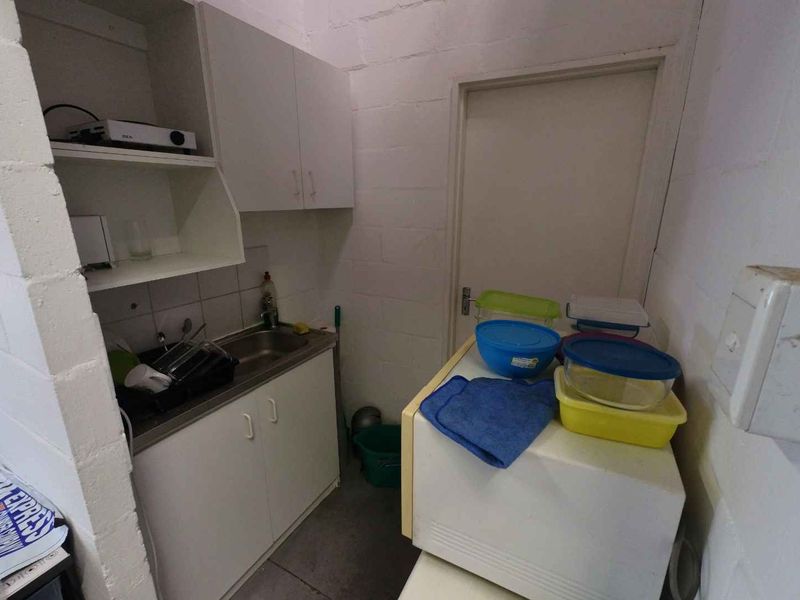 A compact scullery or kitchenette area featuring built-in cabinetry, a stainless steel sink, and exposed blockwork walls.