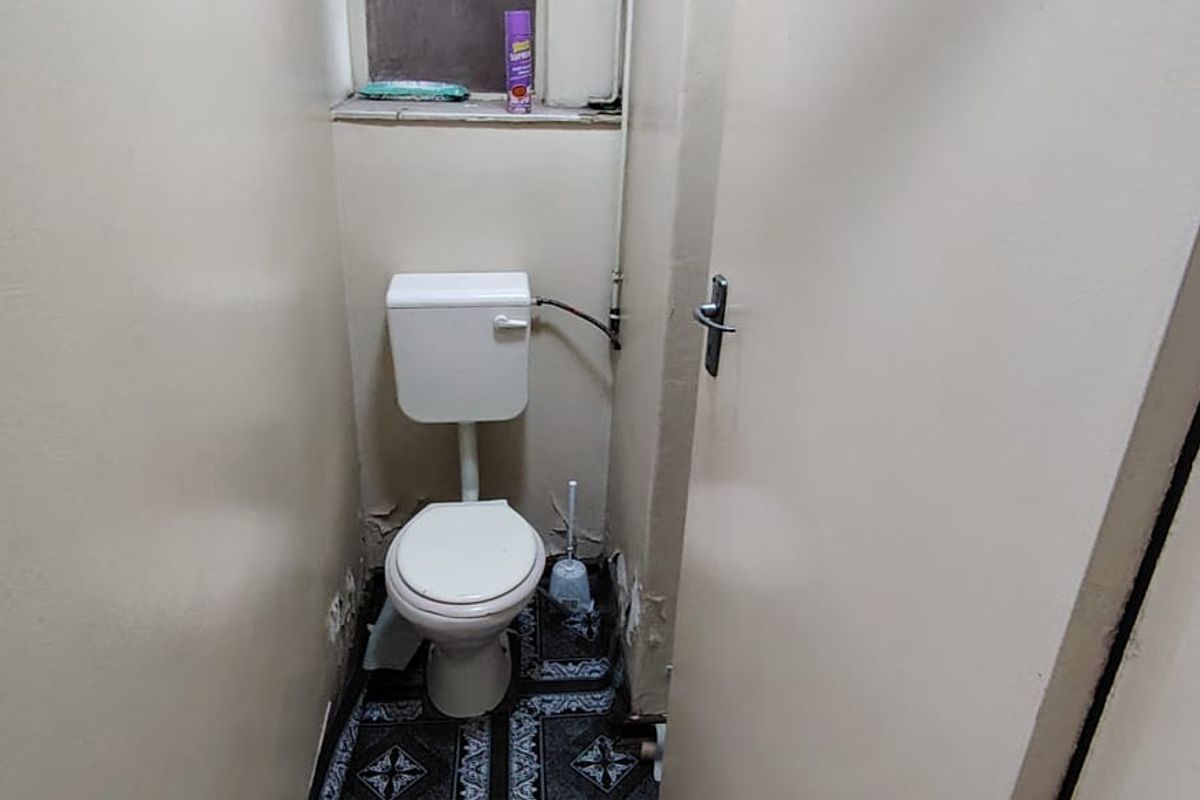 A compact, dated bathroom featuring a standard toilet and basic finishes, currently showing signs of wear and requiring cosmetic updates.