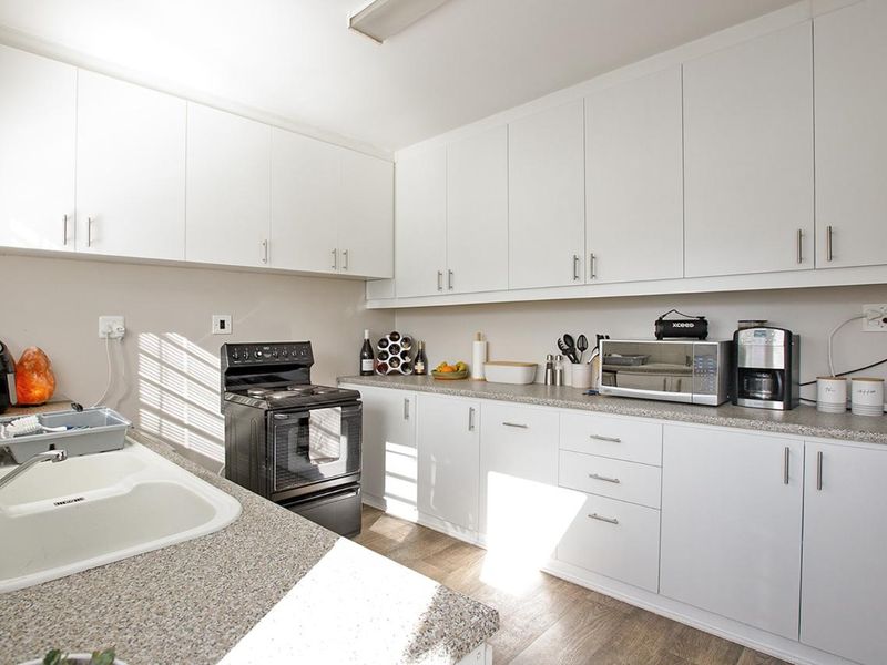 A functional kitchen featuring white cabinetry, laminate countertops, a double basin sink, and a freestanding stove with wood-look laminate flooring.