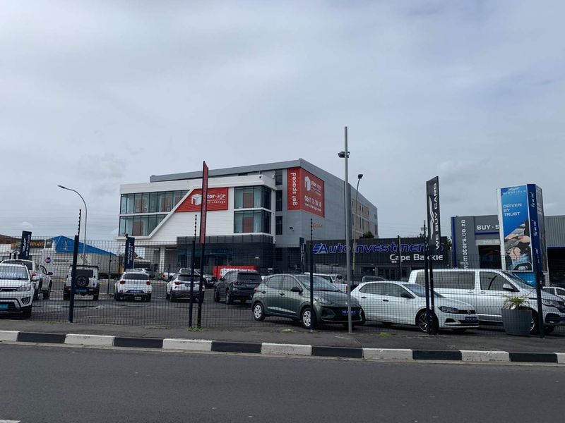 Front view of a commercial retail and storage facility featuring a paved parking lot, perimeter security fencing, and prominent business signage.