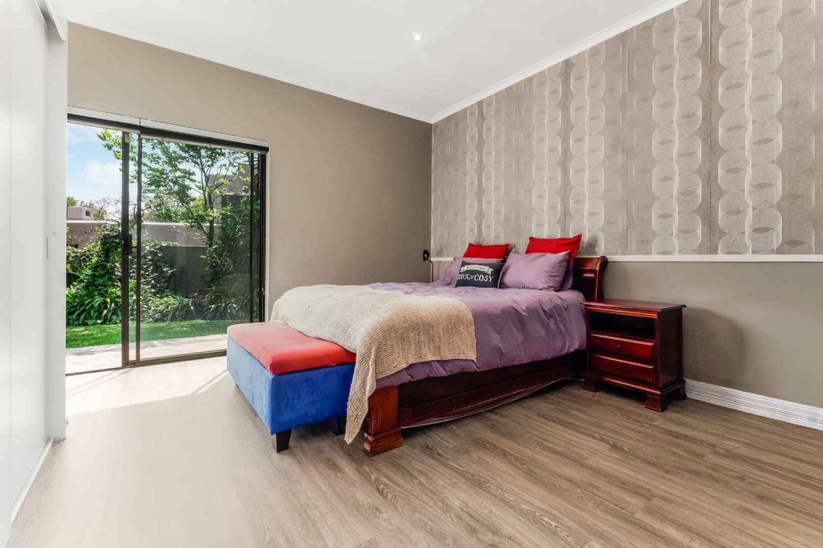 Spacious bedroom featuring modern laminate flooring, a feature wallpaper wall, and a large sliding glass door providing direct access to the garden.