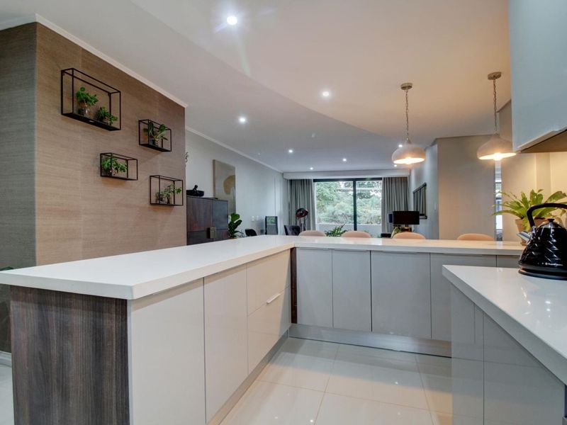 Modern open-plan kitchen featuring sleek cabinetry, quartz countertops, and a central island, seamlessly flowing into the living area with recessed and pendant lighting.