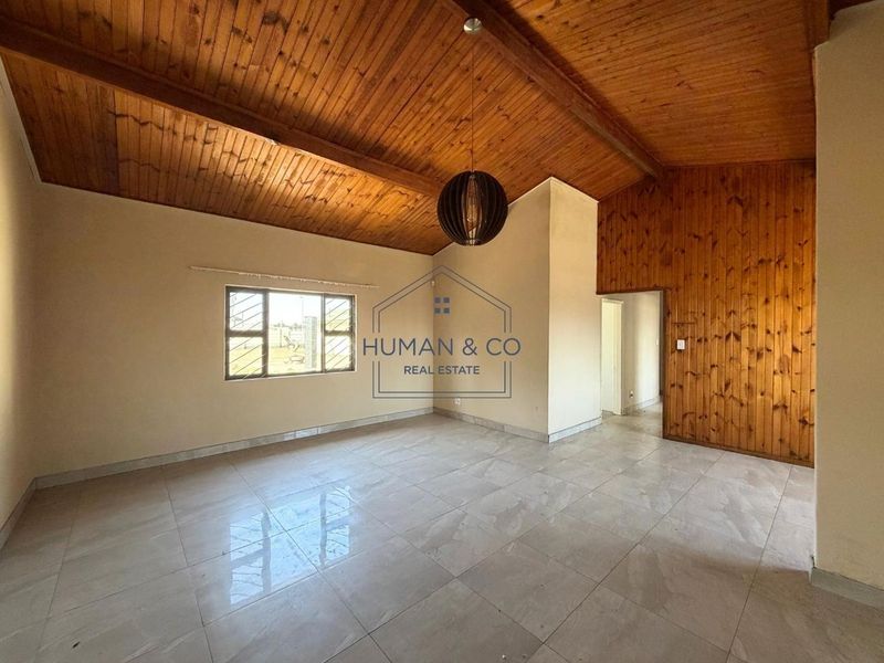 Spacious living area featuring a vaulted timber-clad ceiling, wood-paneled feature wall, and neutral tiled flooring throughout.