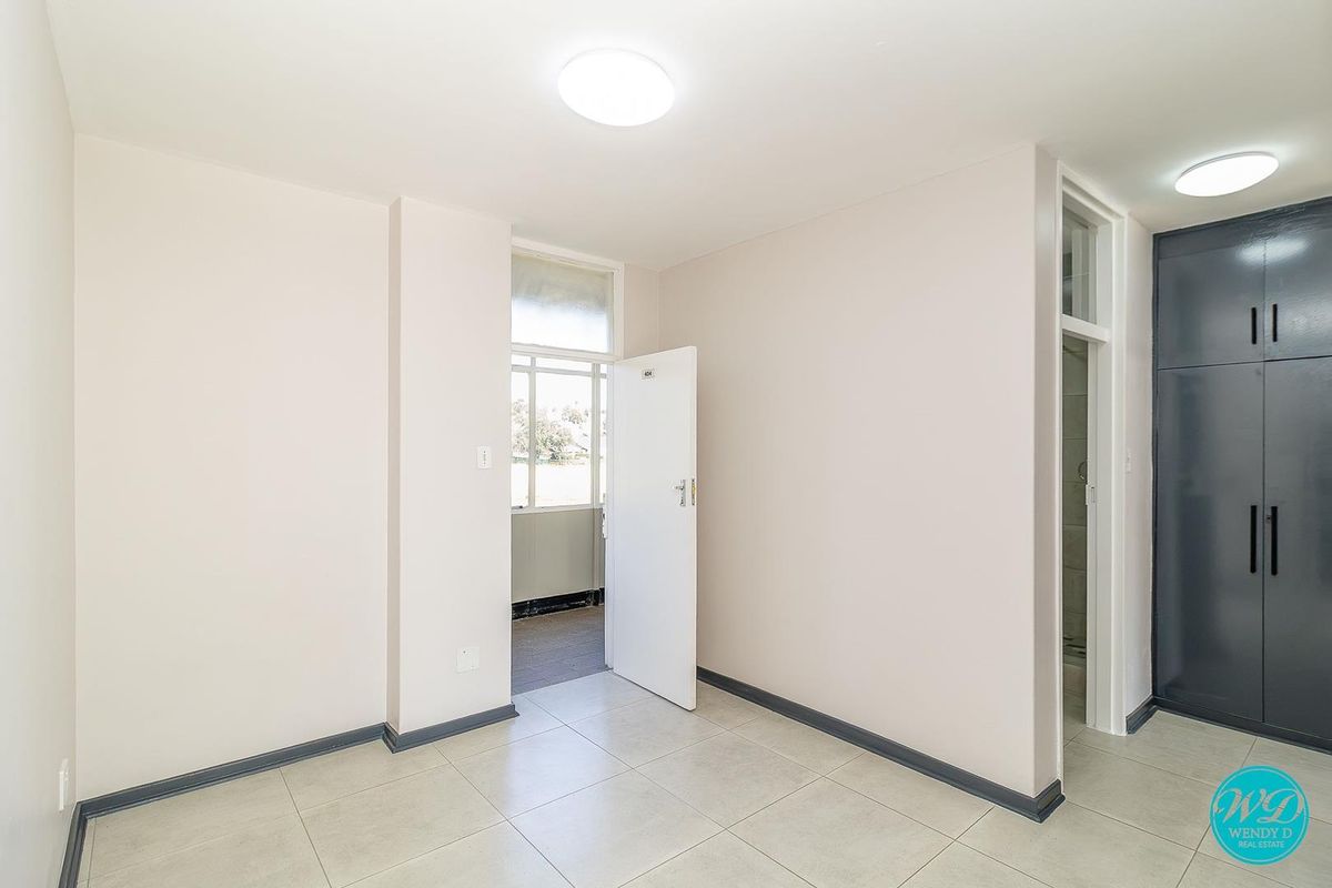 A clean, empty bedroom featuring neutral tiled flooring, built-in storage cupboards, and direct access to an adjoining balcony area.