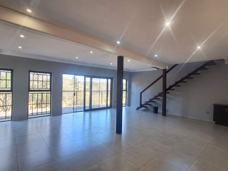 Spacious open-plan living area featuring tiled floors, recessed lighting, a staircase, and large sliding doors leading to an outdoor space.