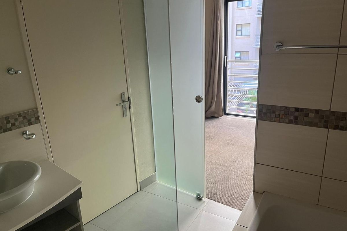 A modern bathroom featuring a vanity with a vessel sink, tiled walls, and a glass door leading to an adjacent carpeted bedroom area.