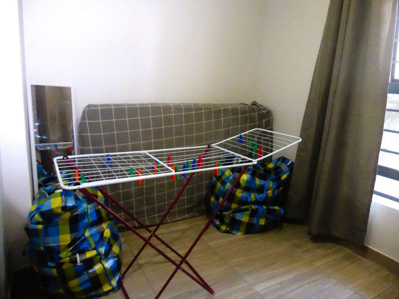 A bedroom space featuring laminate flooring and window curtains, currently utilized for storage and laundry drying.