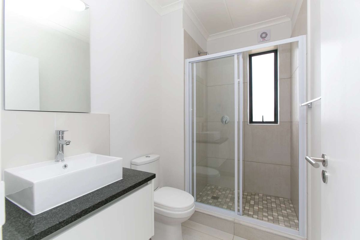 Modern bathroom featuring a sleek vanity with a vessel sink, a glass-enclosed shower with mosaic tile flooring, and a wall-mounted mirror.