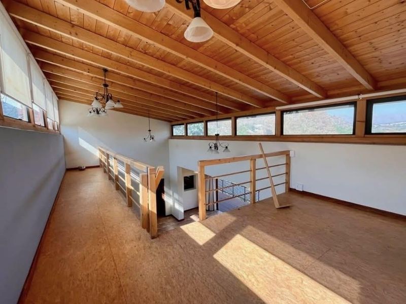 Spacious mezzanine living area featuring exposed timber beam ceilings, clerestory windows, and timber flooring, offering an open and airy atmosphere.