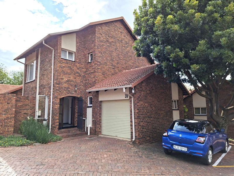 Front elevation of a double-storey facebrick townhouse featuring a single garage, paved driveway, and established garden area.
