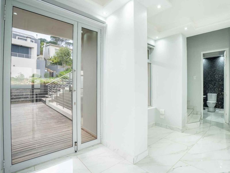 A bright, modern hallway featuring polished marble-look floor tiles, recessed lighting, and a glass door leading to an outdoor deck area.